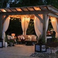 an outdoor living area is lit up with string lights and draping over the couches