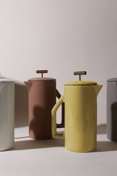 three different colored coffee pots sitting next to each other on a white surface with the lids off