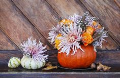 two pumpkins with flowers in them sitting next to each other on a wooden table