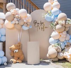 a teddy bear sitting in front of a bunch of balloons on the side of a building