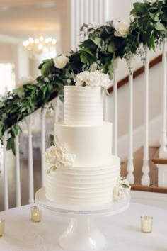 a white wedding cake sitting on top of a table next to candles and greenery