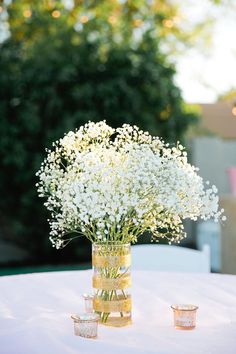 a vase filled with white flowers sitting on top of a table next to two votive cups