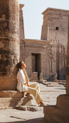 a woman sitting on the steps of an ancient building with columns in front of her