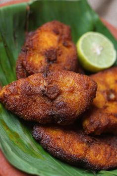 some fried food is on a plate with green leaves and a slice of lime next to it