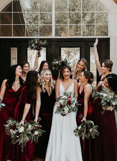 a group of women standing next to each other in front of a door holding bouquets