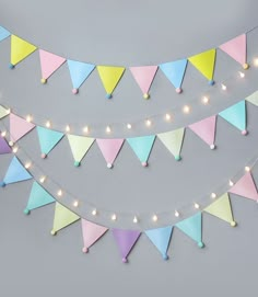 multicolored bunting flags with lights strung from them on a gray wall background