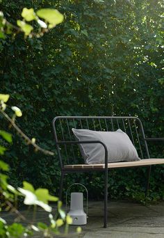 a bench with a pillow on it sitting in front of some bushes and trees,