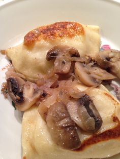 a white plate topped with ravioli covered in mushrooms