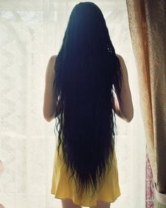 a woman with long black hair standing in front of a window