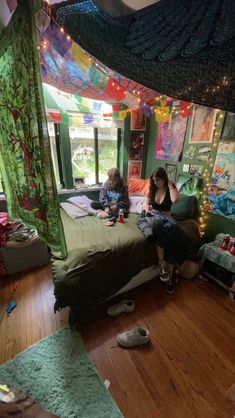 two people sitting on a bed in a room with lots of lights hanging from the ceiling