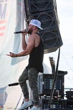 a man standing on top of a stage while holding a microphone in his hand and wearing a white hat