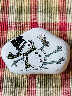 a rock with a snowman painted on it sitting on top of a tablecloth