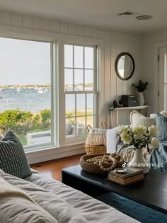 a living room filled with furniture and windows overlooking the water in front of them is a coffee table that has flowers on top of it