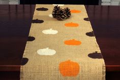 a table runner decorated with pumpkins and pine cone on top of a wooden table