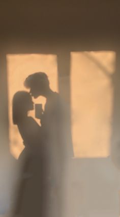 a man and woman standing next to each other in front of a window with the light shining on them