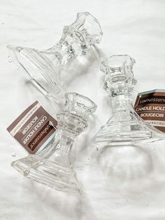 three clear glass candlesticks sitting on top of a white table covered in brown labels