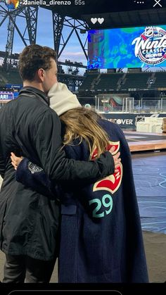 a man and woman embracing each other in front of a large screen at a stadium