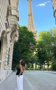 a woman standing in front of the eiffel tower, looking up into the sky