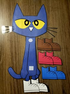 a paper cut out of a blue cat sitting on top of a wooden floor next to shoes