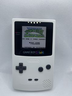 an old nintendo game boy color sitting in front of a white background with the title's logo on it