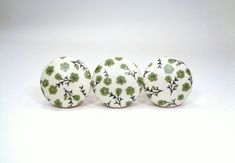 three white balls with green flowers on them sitting next to each other in front of a white background