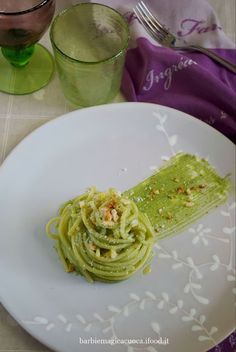 a white plate topped with pasta and pesto sauce next to two glasses of water