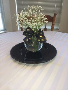 a glass vase with flowers in it sitting on a black plate at the end of a table