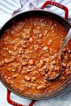 a pot filled with chili and beans on top of a white table cloth next to a spoon