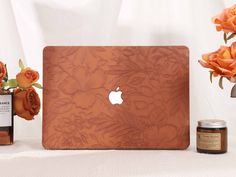 an apple laptop sitting on top of a table next to some flowers and a bottle