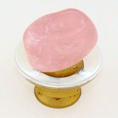 a pink stone sitting on top of a white plate next to a yellow stand with a gold base