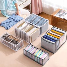 the woman is sitting on the bed with her clothes and other items in plastic bins