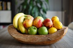 a wooden bowl filled with lots of different types of fruit on top of a table