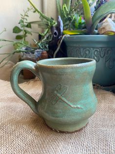 a green mug sitting on top of a table next to some potted planters