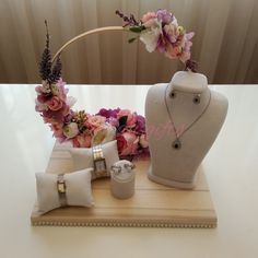 a white vase with flowers and jewelry on a wooden tray next to a necklace holder