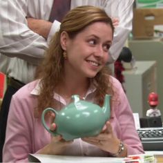 a woman sitting at a desk with a teapot in her hand