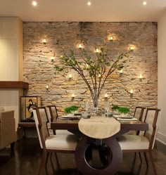 a dining room table and chairs with lights on the wall behind it in front of a stone wall