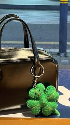 a small green shamrock keychain sitting next to a brown purse on a table