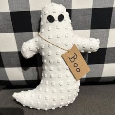 a white stuffed ghost sitting on top of a black and white checkered couch with a tag in it's mouth