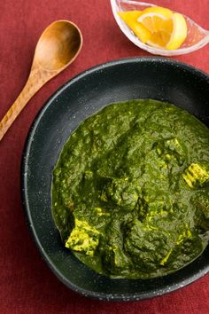 a black bowl filled with green sauce next to a wooden spoon on a red surface