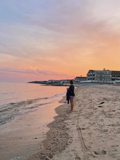 a woman is walking along the beach at sunset