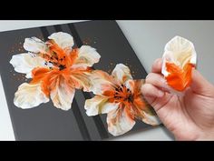 someone is holding an orange and white flower in front of a black painting on the wall