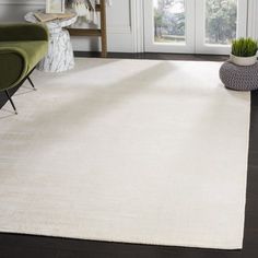 a large white rug in the middle of a living room with two green chairs and a potted plant