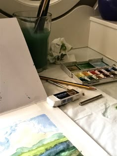 an easel with watercolors and paint on it next to a painting brush