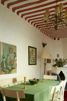 a dining room with green table cloths and white chairs in front of a painting on the wall