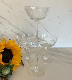 three wine glasses sitting next to a sunflower on a white tablecloth with marble background