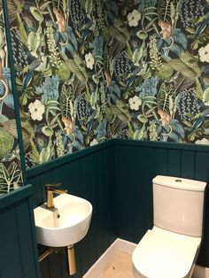 a white toilet sitting next to a sink in a bathroom under a green wallpaper