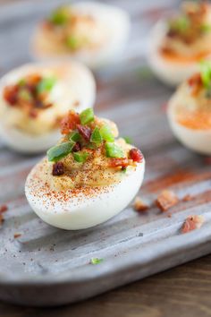 deviled eggs topped with bacon and green onions on a baking sheet, ready to be eaten