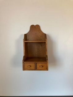 an old wooden shelf with two drawers on the bottom and one drawer below it, against a white wall