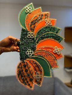 a person holding up an orange and green decorative item in their hand with other decorations on it