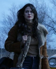 a woman is walking down the street with her hand in her pocket and wearing a fur coat